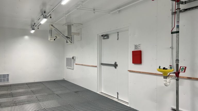 portable laboratory interior with fume snorkle , safety eye wash station and shower, and buss bar over a secondary containment sump